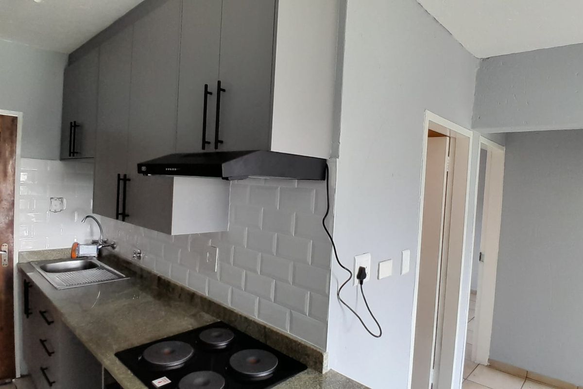 A modern kitchen featuring grey cabinetry, subway tile backsplash, stone countertops, and a built-in electric hob with an extractor fan.