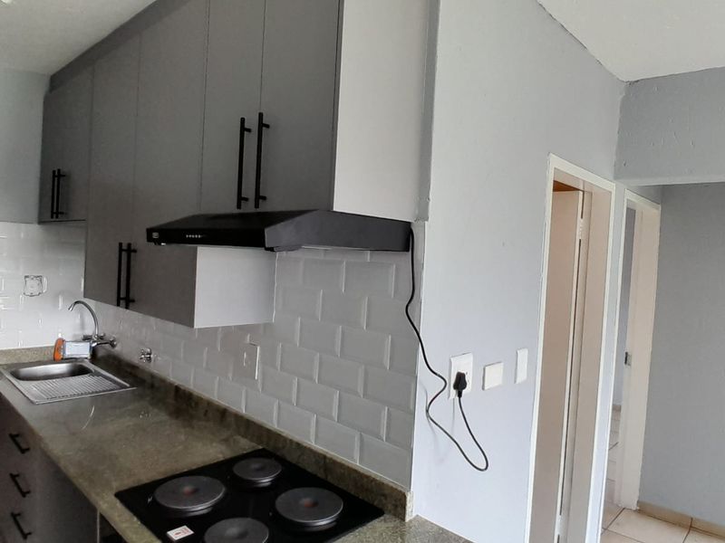 A modern kitchen featuring grey cabinetry, subway tile backsplash, stone countertops, and a built-in electric hob with an extractor fan.
