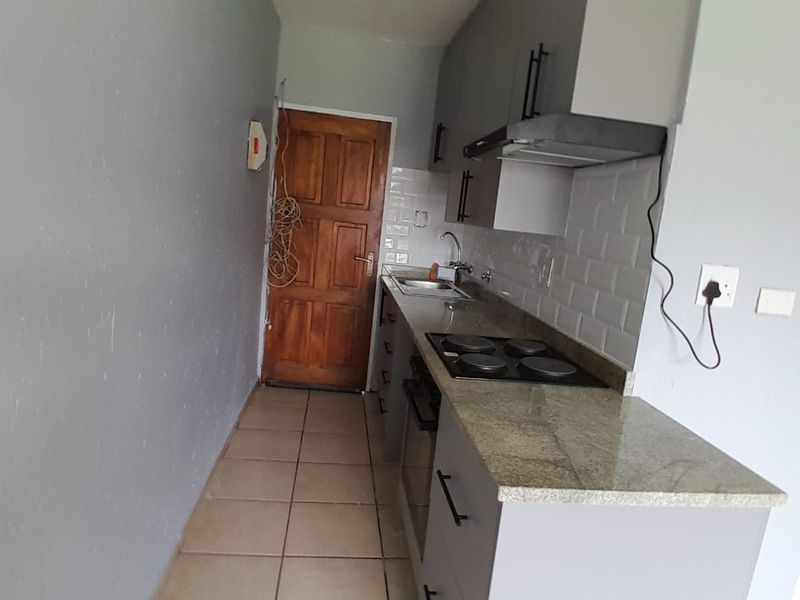 A compact kitchen featuring granite countertops, subway tile backsplash, built-in electric hob, oven, and extractor fan with tiled flooring.