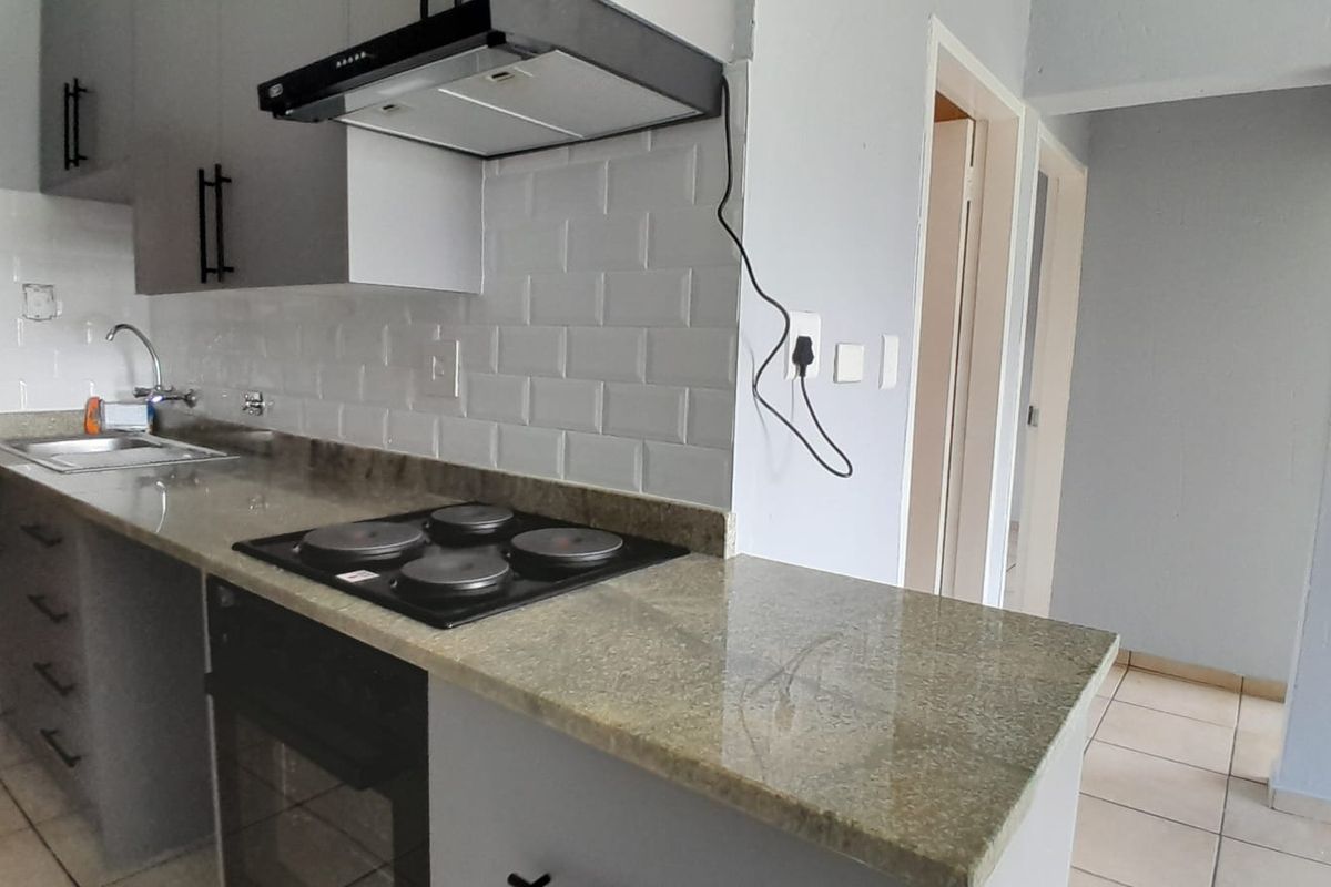 A modern kitchen featuring granite countertops, subway tile backsplash, built-in oven, electric hob, and ample cabinetry, presenting a clean and functional workspace.