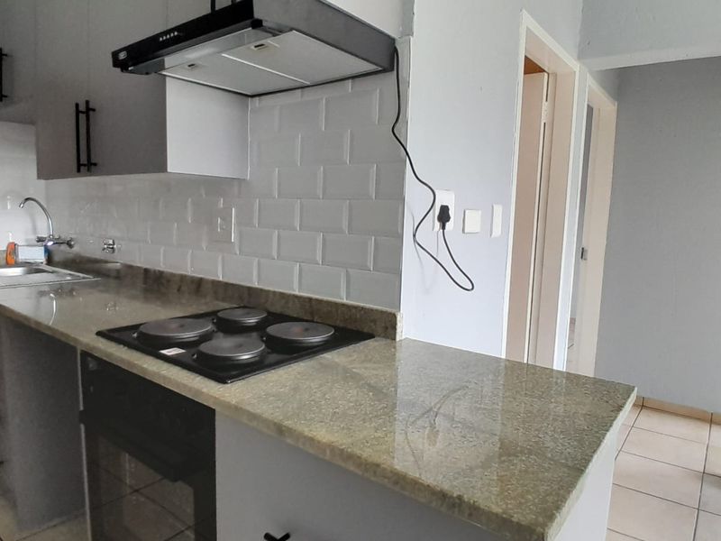 A modern kitchen featuring granite countertops, subway tile backsplash, built-in oven, electric hob, and ample cabinetry, presenting a clean and functional workspace.