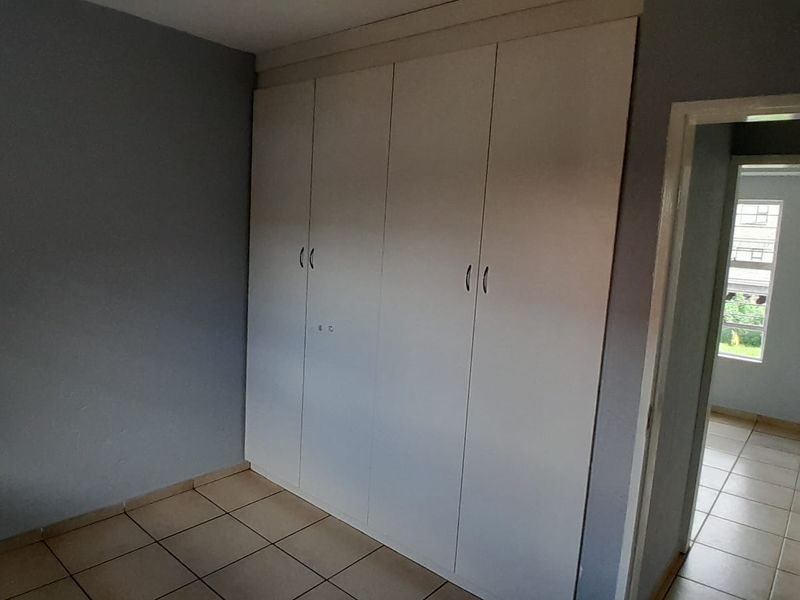 A clean, empty bedroom featuring neutral wall paint, tiled flooring, and ample built-in cupboard storage space.
