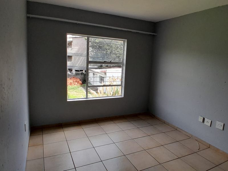 An empty bedroom featuring tiled flooring, grey painted walls, and an aluminium window frame, providing a blank canvas for potential interior design.