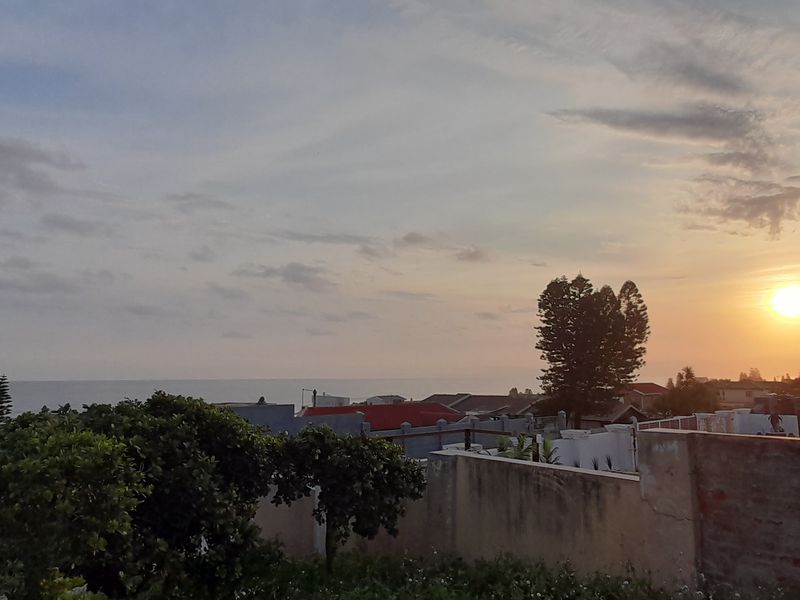 A scenic coastal view overlooking the neighborhood and ocean at sunset, featuring a residential boundary wall and partial view of a tiled roof structure.