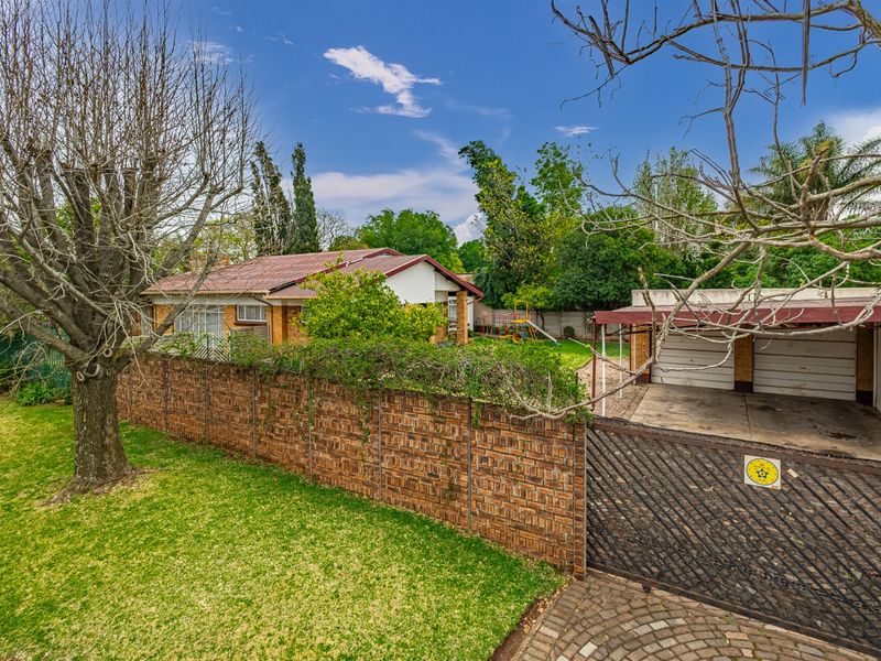 Front view of a residential property featuring a brick boundary wall, metal gate, paved driveway, and a double garage with a tiled roof.
