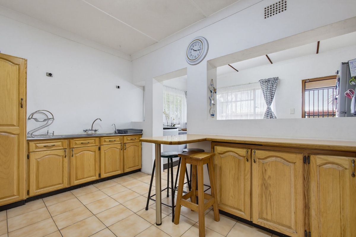A functional kitchen featuring wooden cabinetry, tiled flooring, and a convenient breakfast bar with a pass-through window connecting to the adjacent living space.