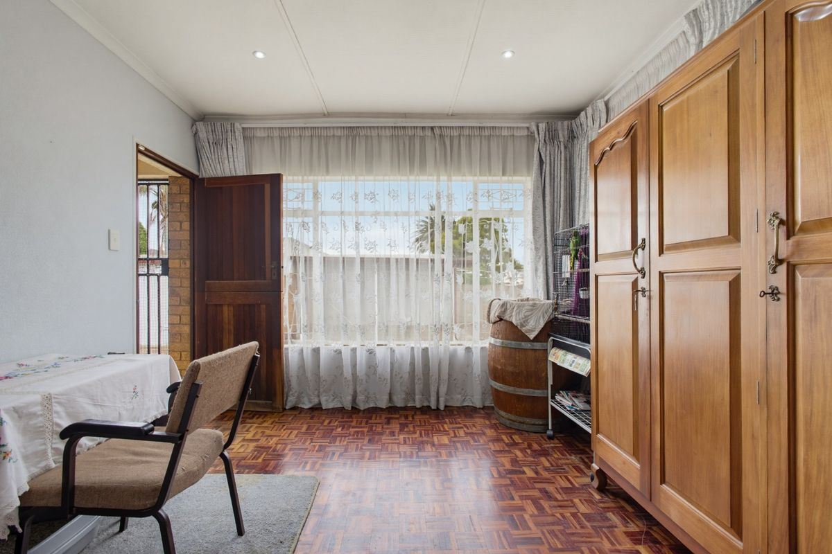 A bedroom featuring classic parquet flooring, recessed downlighting, and a large window providing natural light.