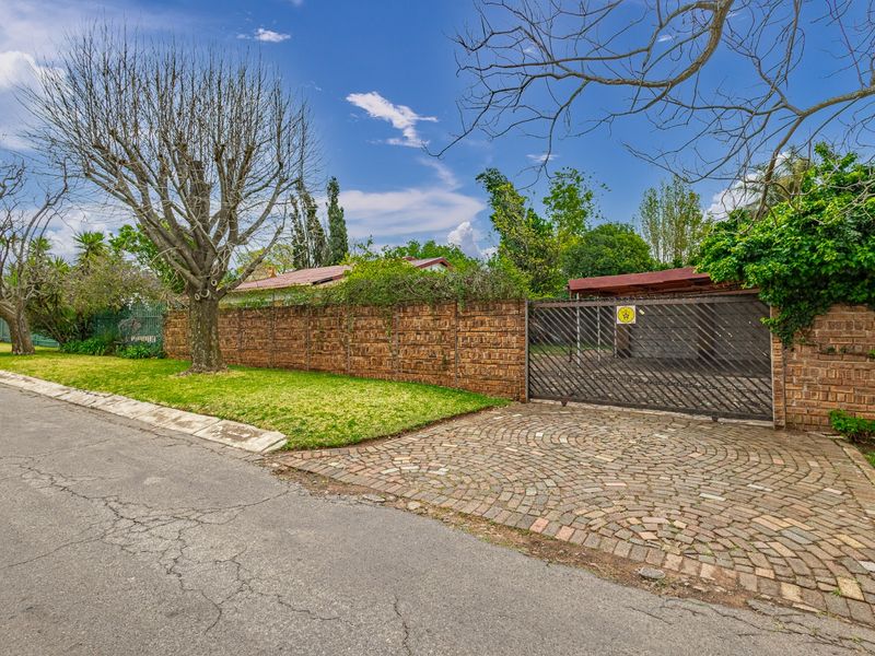 Front exterior view of the property featuring a brick boundary wall, cobblestone driveway, and a secure metal sliding gate leading to a carport.