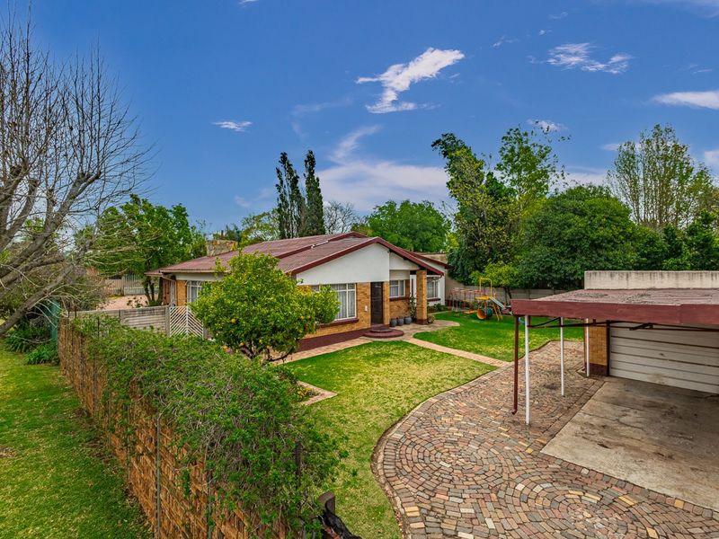 A view of the front exterior featuring a brick driveway, carport, and a well-maintained garden with a brick boundary wall.