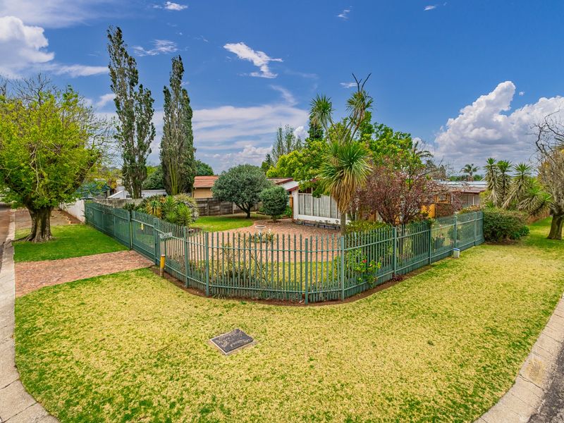 A corner property featuring a well-maintained garden, brick paved driveway, and secure metal perimeter fencing, offering good street appeal.