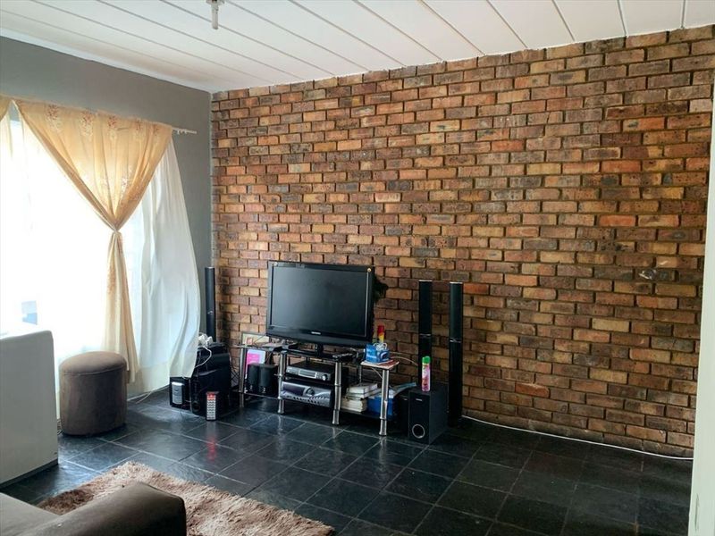 Living room featuring a prominent exposed brick feature wall, dark tiled flooring, and a panelled ceiling.