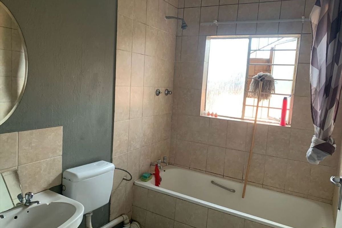 A functional bathroom featuring a bathtub with shower head, basin, and toilet, finished with tiled walls and security bars on the window.