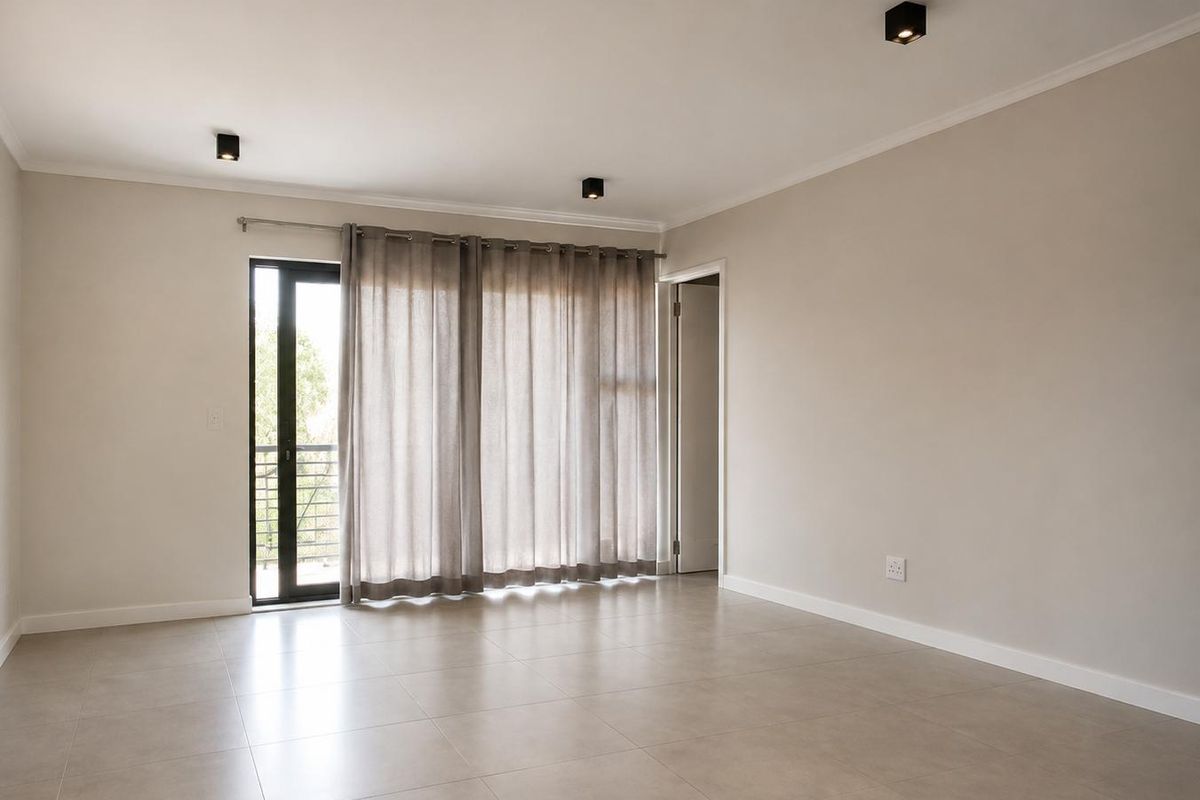 A bright, empty living room featuring neutral tiled flooring, modern recessed ceiling lights, and a sliding glass door leading to a balcony.