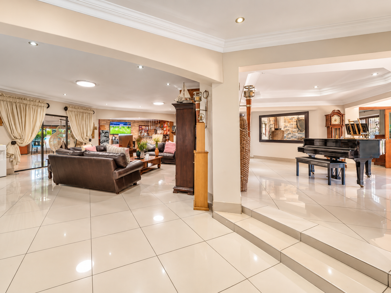 Spacious open-plan living area featuring polished porcelain tiles, recessed lighting, and a raised platform section, creating a seamless flow between lounge and entertainment spaces.
