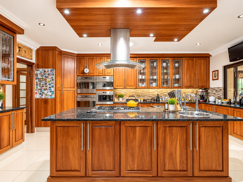 A well-appointed kitchen featuring warm wooden cabinetry, granite countertops, a central island with a gas hob, and integrated stainless steel appliances.