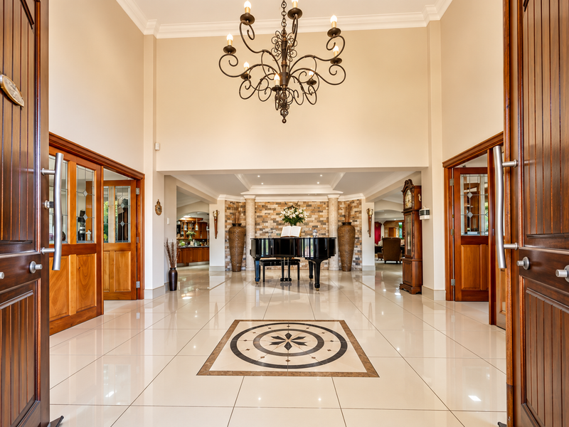 Grand entrance hall featuring high ceilings, a wrought iron chandelier, polished porcelain flooring with a decorative inlay, and a stone feature wall.