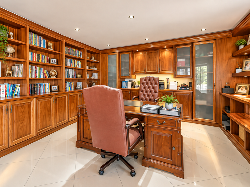 A professional home office featuring extensive custom-built wooden cabinetry, integrated shelving, recessed lighting, and polished tiled flooring.