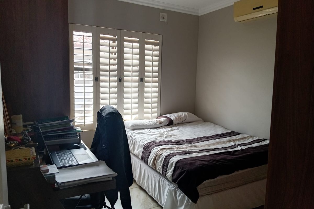 A functional bedroom featuring tiled flooring, plantation shutters for light control, and a wall-mounted split-system air conditioner.