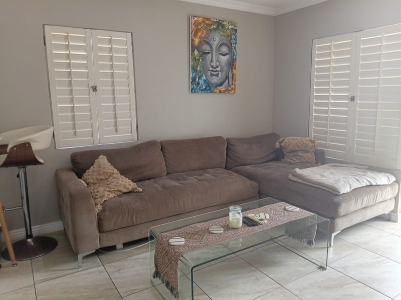 A comfortable living room featuring neutral tiled flooring, crown molding, and white plantation shutters that provide adjustable natural light control.