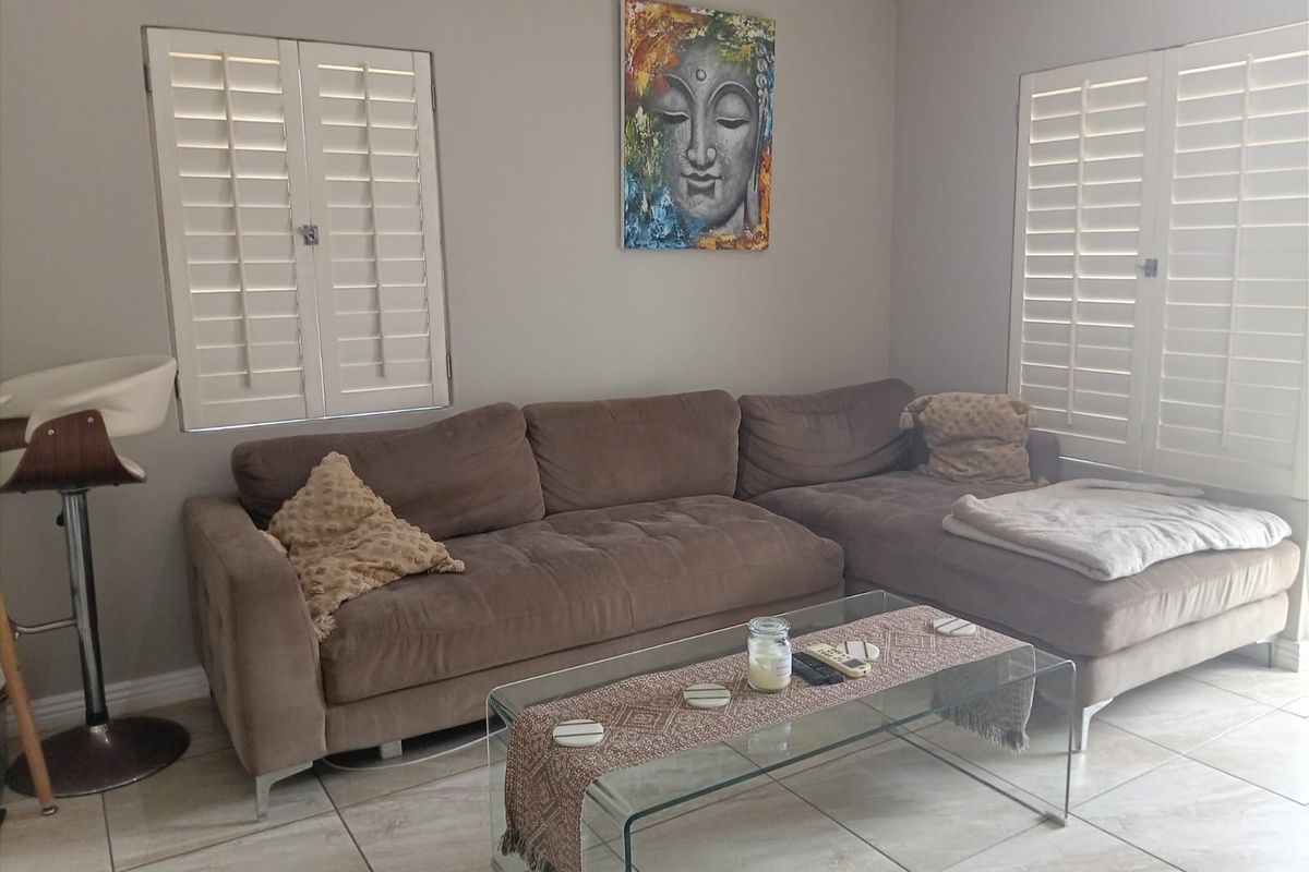 A comfortable living room featuring neutral tiled flooring, crown molding, and white plantation shutters that provide adjustable natural light control.