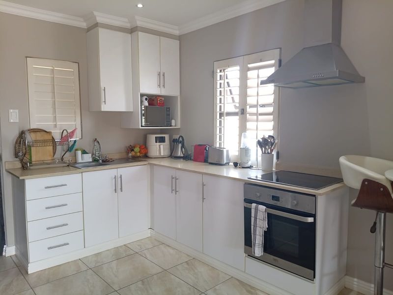 A well-maintained kitchen featuring white cabinetry, stainless steel appliances including an oven and extractor fan, tiled flooring, and plantation shutters.