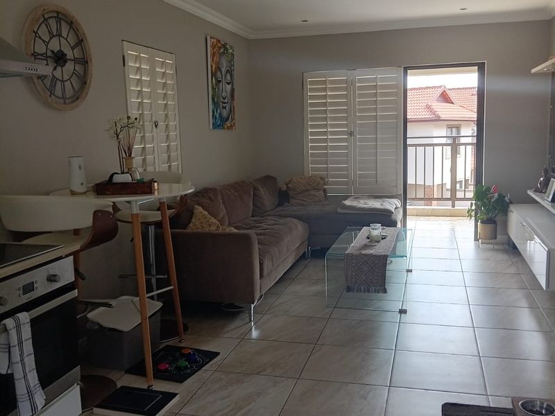 Open-plan living area featuring tiled flooring, recessed lighting, and integrated kitchen appliances, with direct access to a private balcony through shuttered doors.
