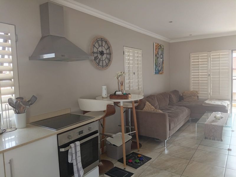 Open-plan living area featuring a modern kitchen with built-in oven, hob, and extractor fan, complemented by tiled flooring and plantation shutters throughout.