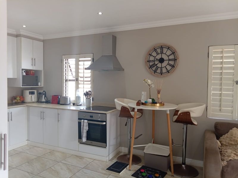 Modern open-plan kitchen featuring white cabinetry, stainless steel appliances, tiled flooring, and plantation shutters, seamlessly integrated with a compact dining area.