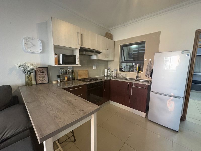 Compact kitchen featuring built-in cabinetry, granite countertops, integrated hob and oven, and tiled flooring, providing a functional and efficient cooking space.