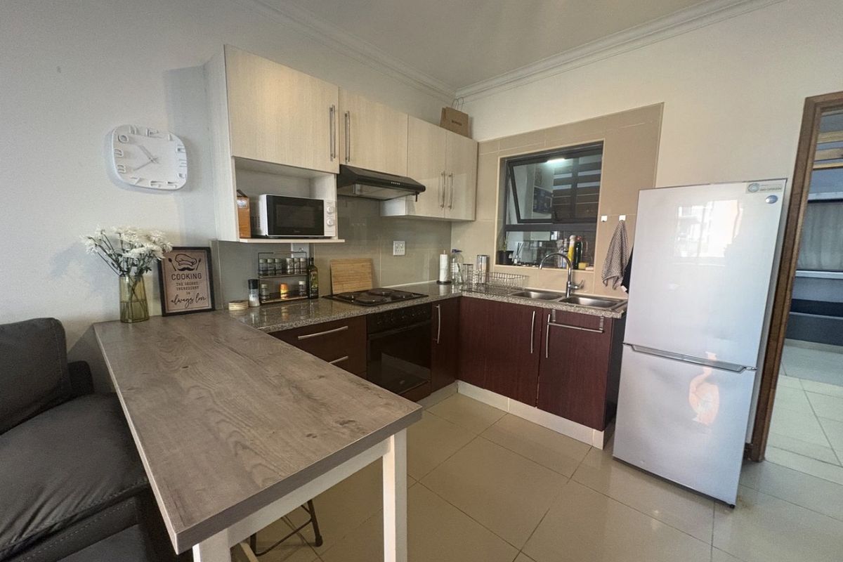 Compact kitchen featuring built-in cabinetry, granite countertops, integrated hob and oven, and tiled flooring, providing a functional and efficient cooking space.