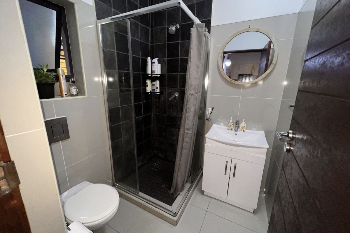 Modern bathroom featuring a glass-enclosed shower, wall-mounted toilet, and a white vanity cabinet with a basin, finished with neutral and dark accent tiling.