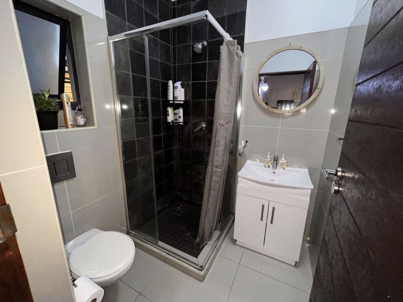 Modern bathroom featuring a glass-enclosed shower, wall-mounted toilet, and a white vanity cabinet with a basin, finished with neutral and dark accent tiling.