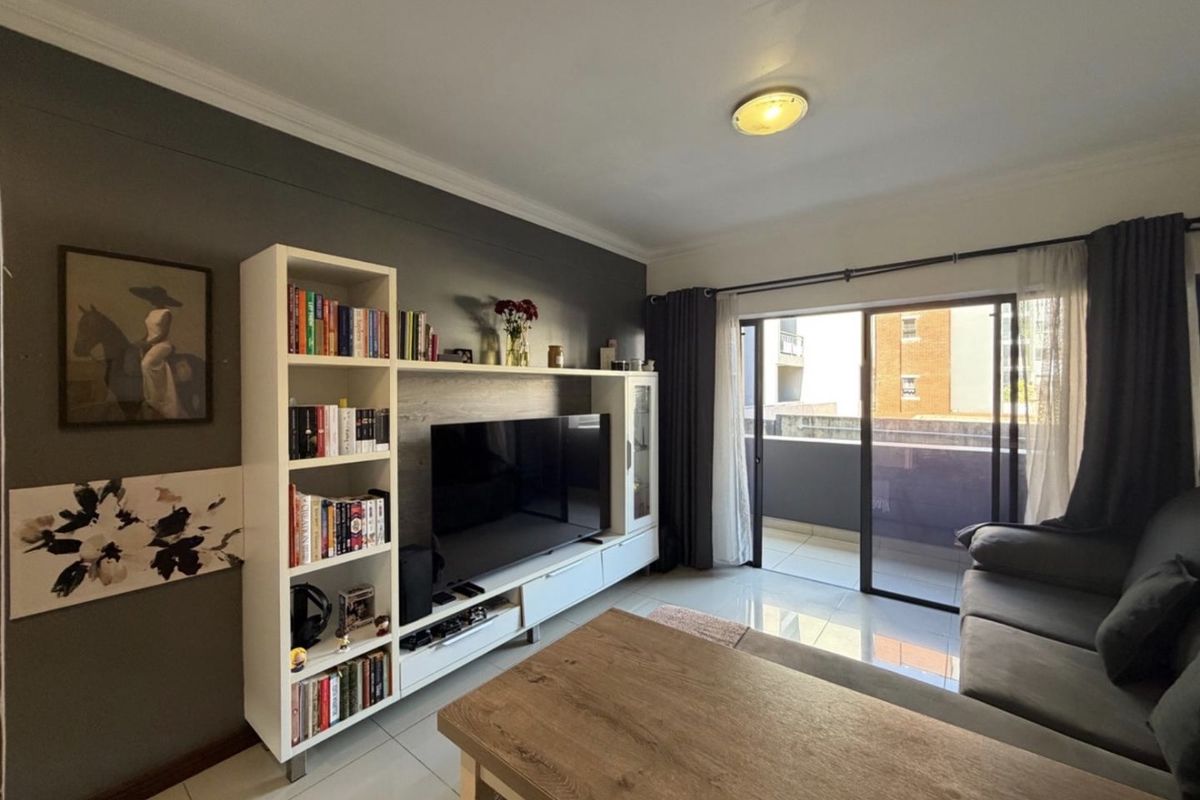 A well-maintained living room featuring tiled flooring, a feature wall, and a large sliding glass door providing access to an outdoor balcony area.