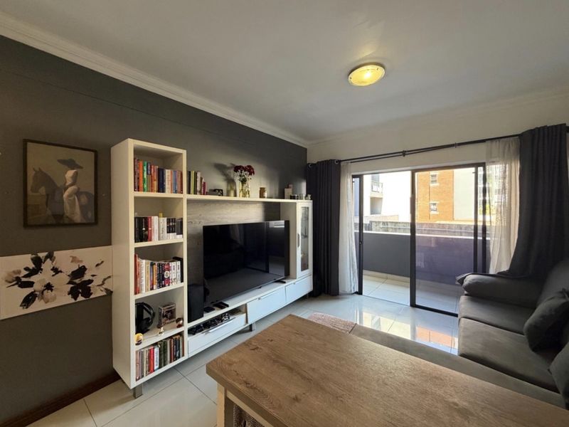 A well-maintained living room featuring tiled flooring, a feature wall, and a large sliding glass door providing access to an outdoor balcony area.