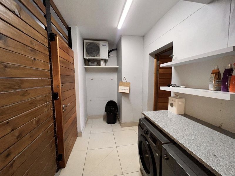 A functional laundry area featuring tiled flooring, stone countertop workspace, floating shelving, and a timber slat partition wall.
