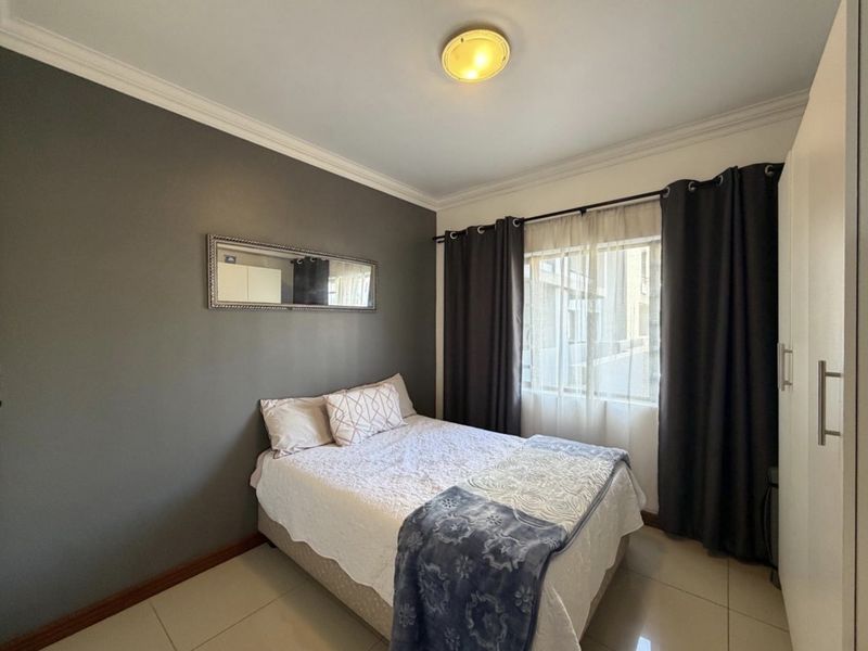 A well-maintained bedroom featuring tiled flooring, a built-in wardrobe, and a neutral grey accent wall with decorative ceiling cornicing.