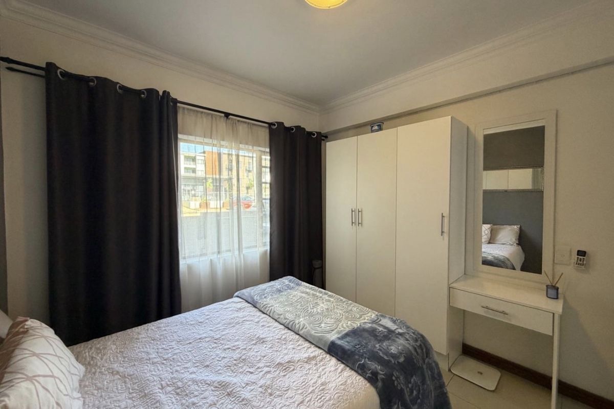 A functional bedroom featuring a built-in wardrobe, tiled flooring, and decorative ceiling cornice, offering a clean and practical living space.