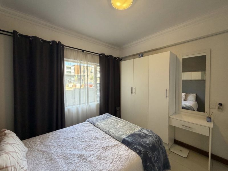 A functional bedroom featuring a built-in wardrobe, tiled flooring, and decorative ceiling cornice, offering a clean and practical living space.