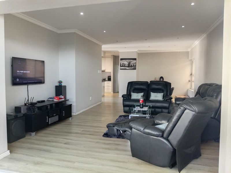 Spacious open-plan living area featuring modern laminate flooring, recessed downlighting, and a seamless transition into the adjacent kitchen space.