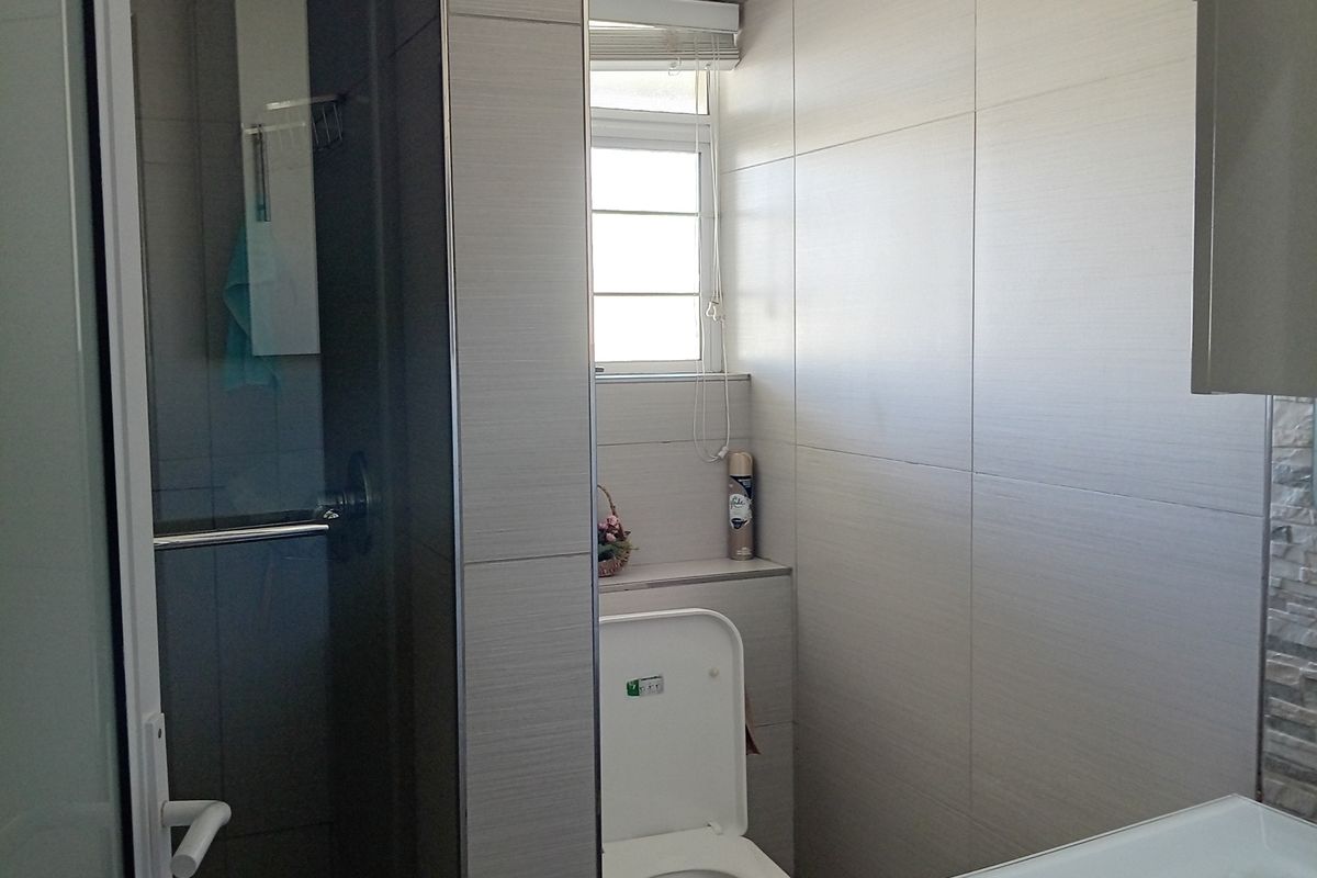 A modern bathroom featuring a glass-enclosed shower, a wall-mounted toilet, and a vanity unit with neutral-toned wall and floor tiles.