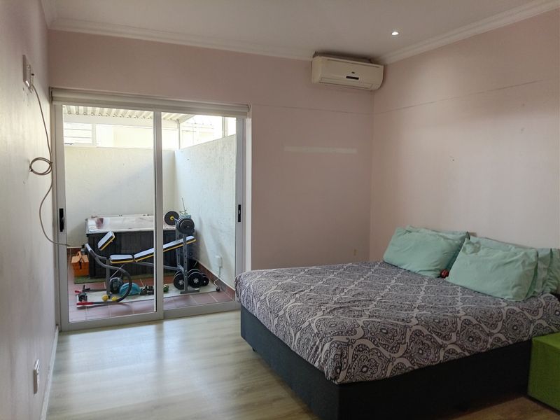 Bedroom featuring laminate flooring, split-system air conditioning, and direct access to a private patio area through sliding glass doors.