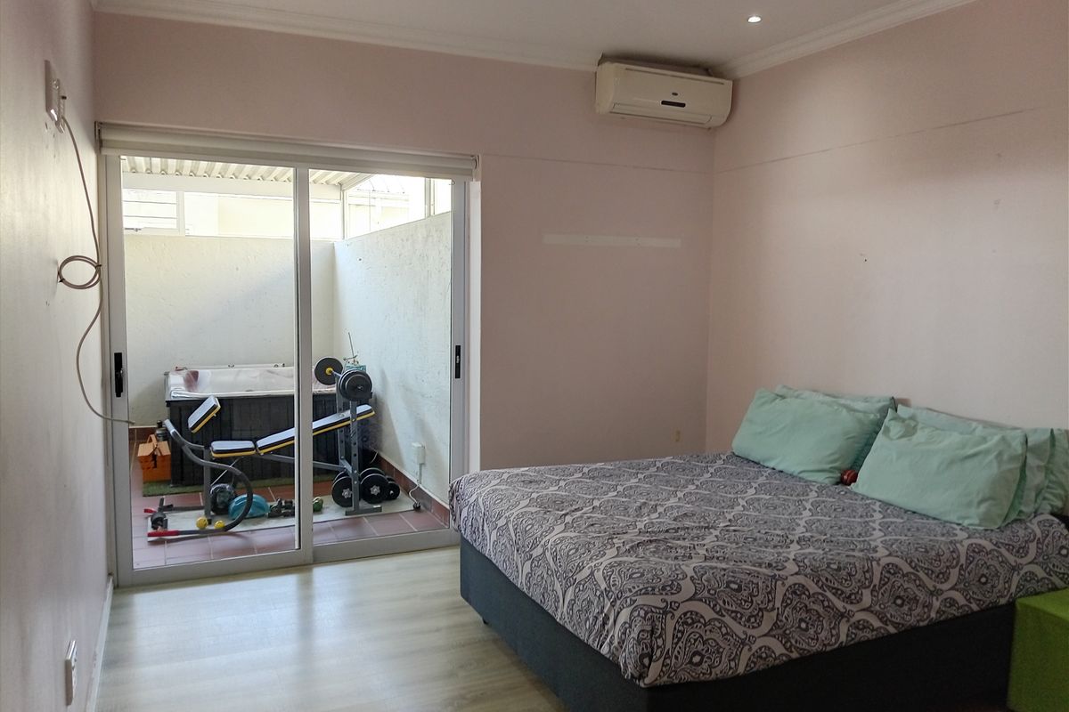 Bedroom featuring laminate flooring, split-system air conditioning, and direct access to a private patio area through sliding glass doors.