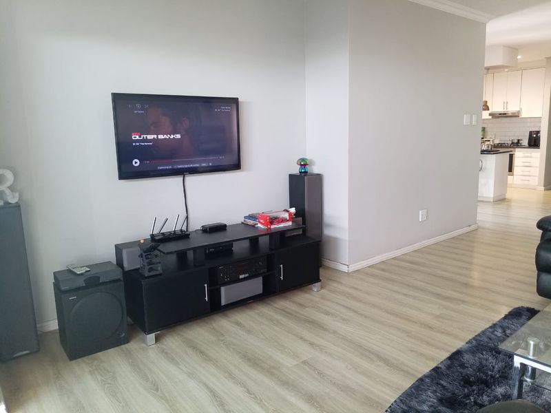 Open plan living area featuring light wood-look laminate flooring, flowing into a modern kitchen with white cabinetry and tiled backsplash.