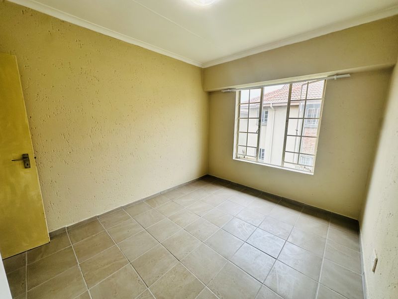 An empty bedroom featuring tiled flooring, textured walls, and a steel-framed window, offering a blank canvas for potential interior updates.