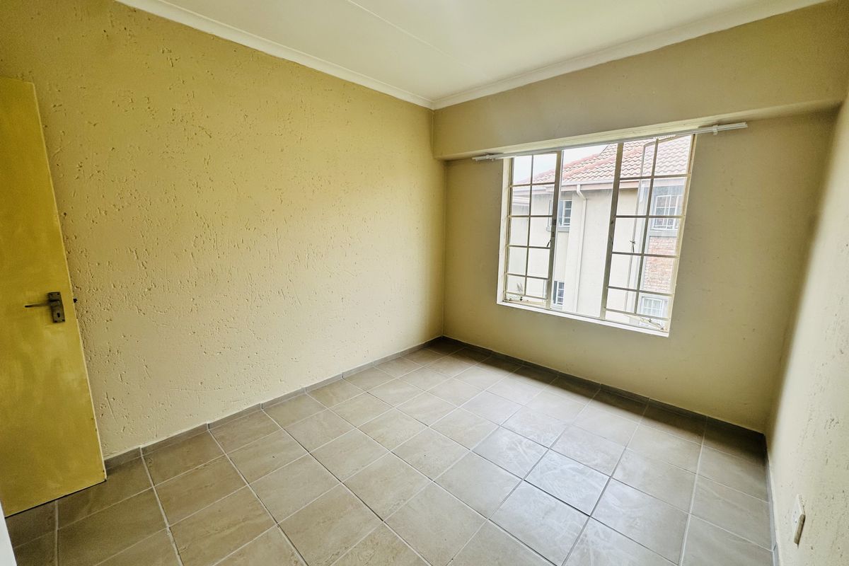 An empty bedroom featuring tiled flooring, textured walls, and a steel-framed window, offering a blank canvas for potential interior updates.