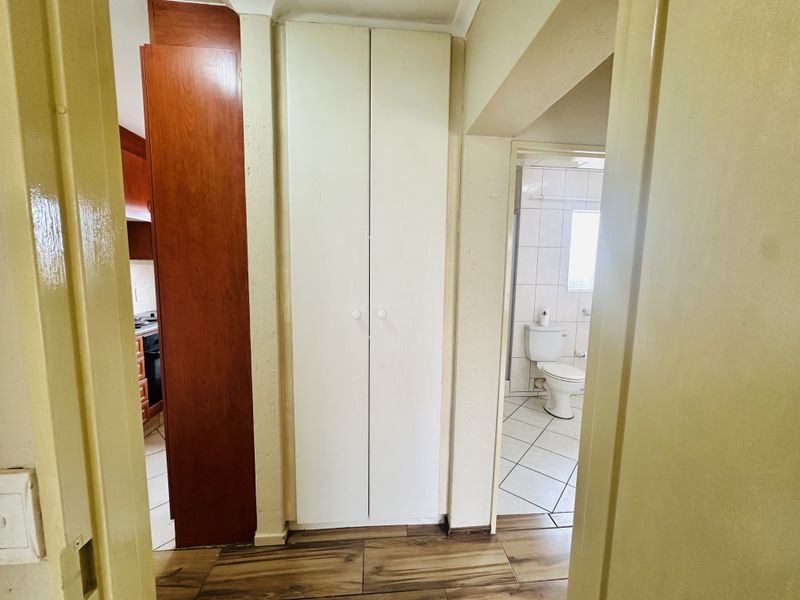 A hallway featuring wood-look floor tiles, a built-in storage cupboard, and views into the adjacent kitchen and bathroom areas.