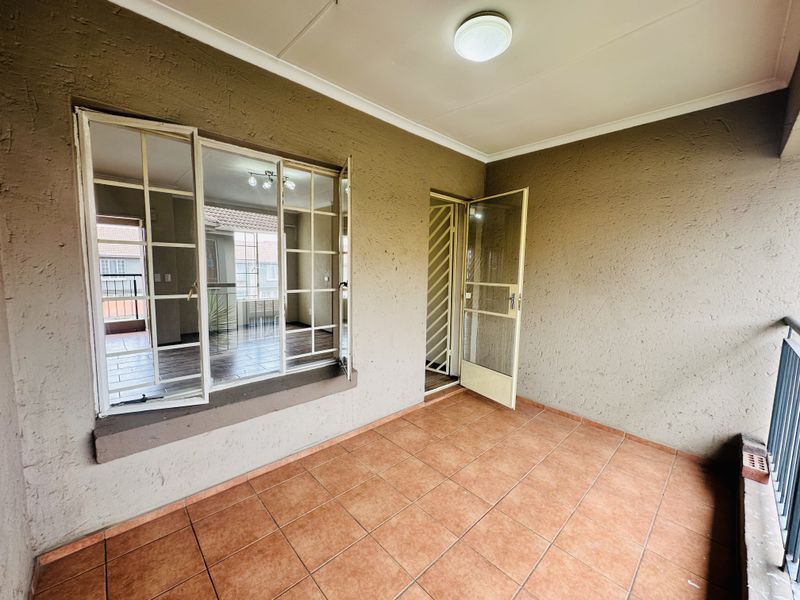 A covered balcony featuring tiled flooring, textured walls, and a metal security gate, providing an outdoor extension to the living area.
