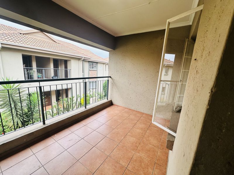 A covered balcony featuring tiled flooring and a metal balustrade, offering an outdoor space with views of the surrounding apartment complex.