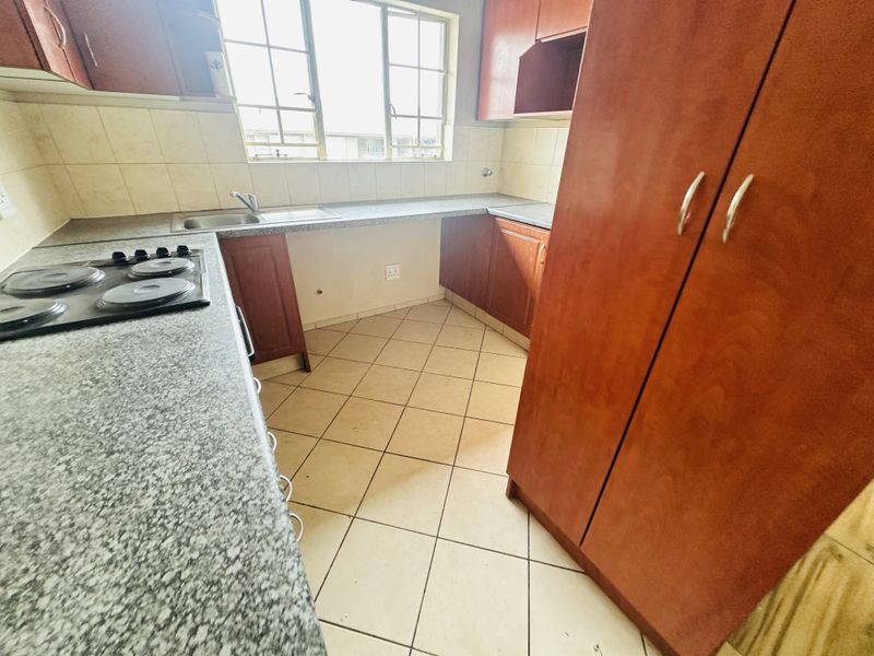 A functional kitchen featuring built-in wooden cabinetry, granite countertops, a stainless steel sink, and an electric hob with tiled backsplash and flooring.