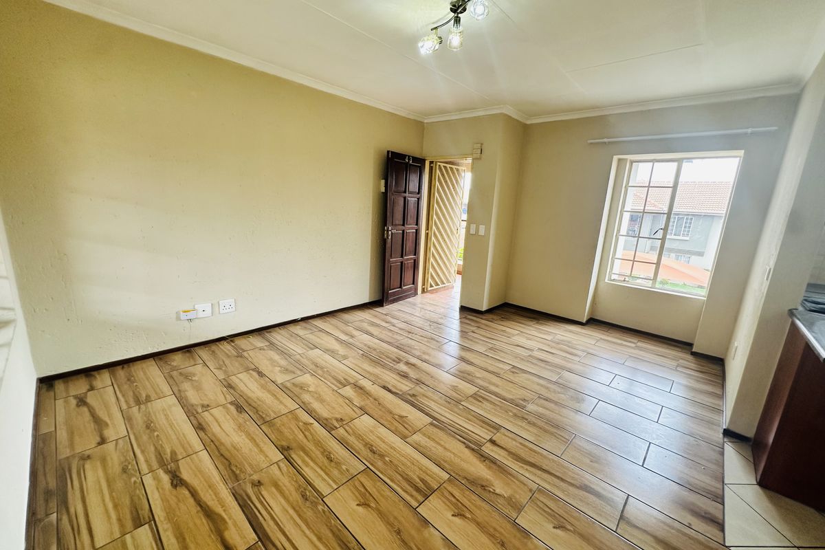 An empty living room featuring wood-look tile flooring, a security gate, and natural light from a casement window.